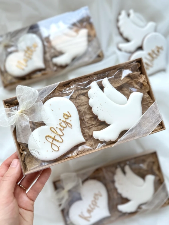 Zestaw prezentowy ręcznie zdobionych pierników na chrzest. Pierniki w kształcie serca z personalizowanym imieniem i gołąbkiem zapakowane w ozdobne pudełko przewiązane kokardką