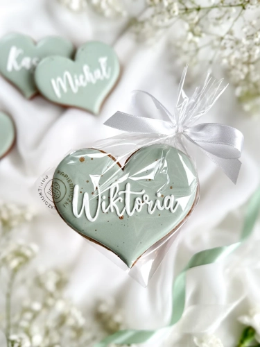 Piernik na komunię w kształcie serca z imieniem zapakowany w celofanowy woreczek z kokardką jako forma podziękowania dla gości komunijnych