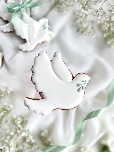 Piernik na komunię w kształcie gołąbka z gałązką zapakowany w celofanowy woreczek z kokardką jako forma podziękowania dla gości komunijnych