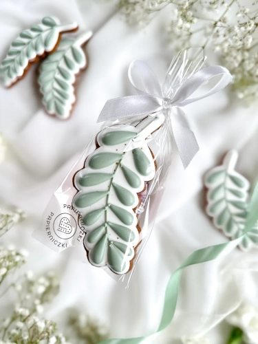 Piernik na komunię w kształcie gałązki oliwnej zapakowany w celofanowy woreczek z kokardką jako forma podziękowania dla gości komunijnych