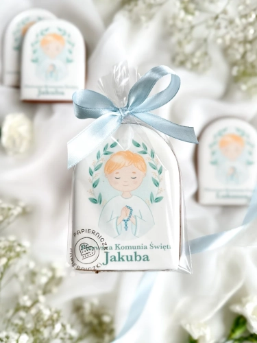 Piernik na komunię z grafiką chłopca i personalizowanym napisem zapakowany w celofanowy woreczek z kokardką jako forma podziękowania dla gości komunijnych