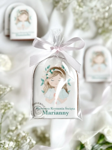Piernik na komunię z grafiką dziewczynki i personalizowanym napisem zapakowany w celofanowy woreczek z kokardką jako forma podziękowania dla gości komunijnych