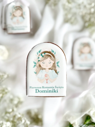 Piernik na komunię z grafiką dziewczynki i personalizowanym napisem zapakowany w celofanowy woreczek z kokardką jako forma podziękowania dla gości komunijnych