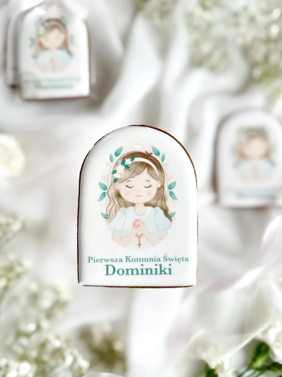 Piernik na komunię z grafiką dziewczynki i personalizowanym napisem zapakowany w celofanowy woreczek z kokardką jako forma podziękowania dla gości komunijnych