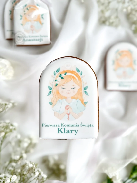 Piernik na komunię z grafiką dziewczynki i personalizowanym napisem zapakowany w celofanowy woreczek z kokardką jako forma podziękowania dla gości komunijnych
