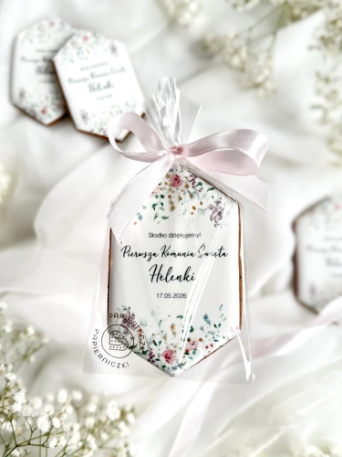 Piernik na komunię w kształcie plakietki z grafiką polnych kwiatów, złoceniem i personalizowanym napisem zapakowany w celofanowy woreczek z kokardką jako forma podziękowania dla gości komunijnych