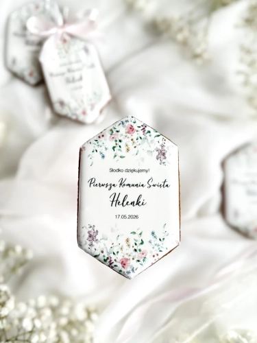Piernik na komunię w kształcie plakietki z grafiką polnych kwiatów, złoceniem i personalizowanym napisem zapakowany w celofanowy woreczek z kokardką jako forma podziękowania dla gości komunijnych